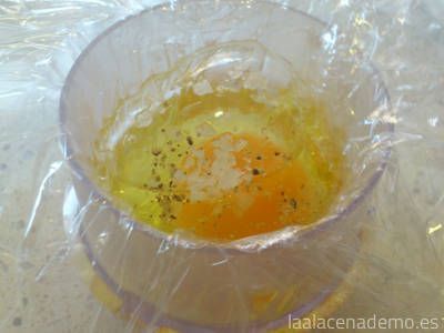 Coloca film transparente en el cubilete, vierte el huevo con un poco de sal y pimienta